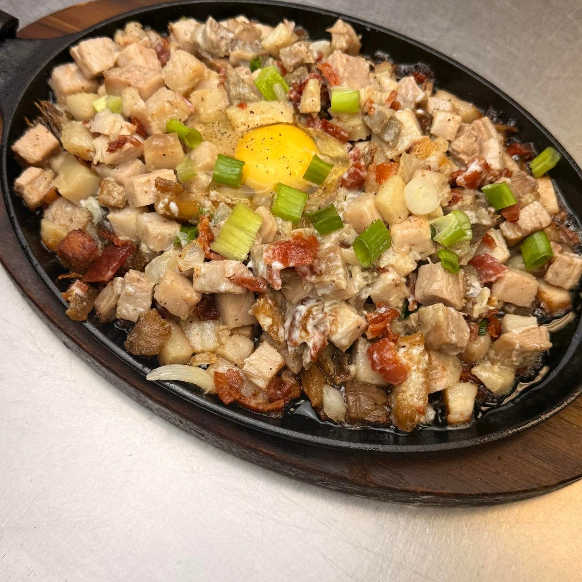 90° Café Pork Sisig on a sizzling platter, topped with egg and green onions