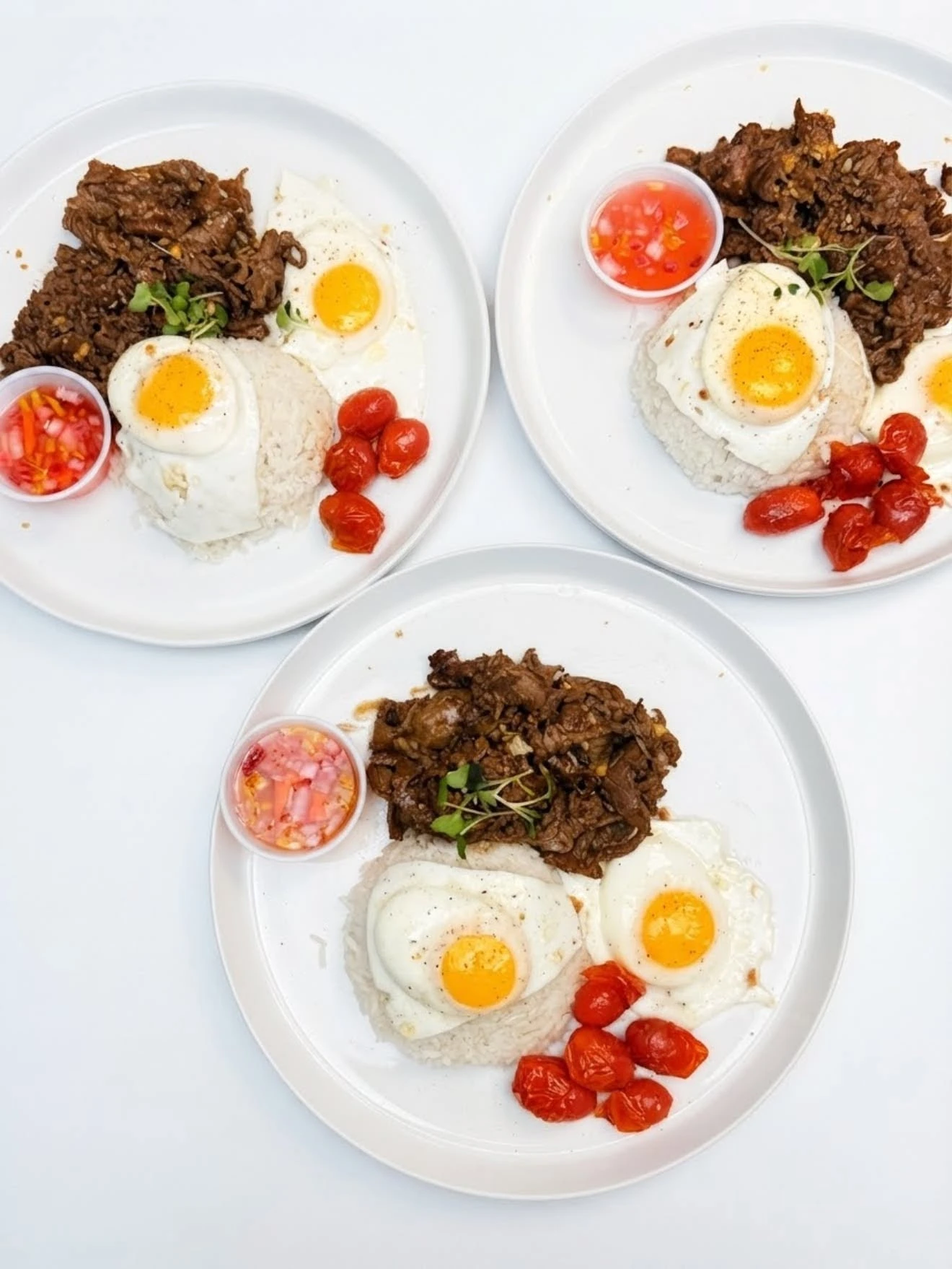 90° Café tapsilog with fried eggs, beef and rice on white plates