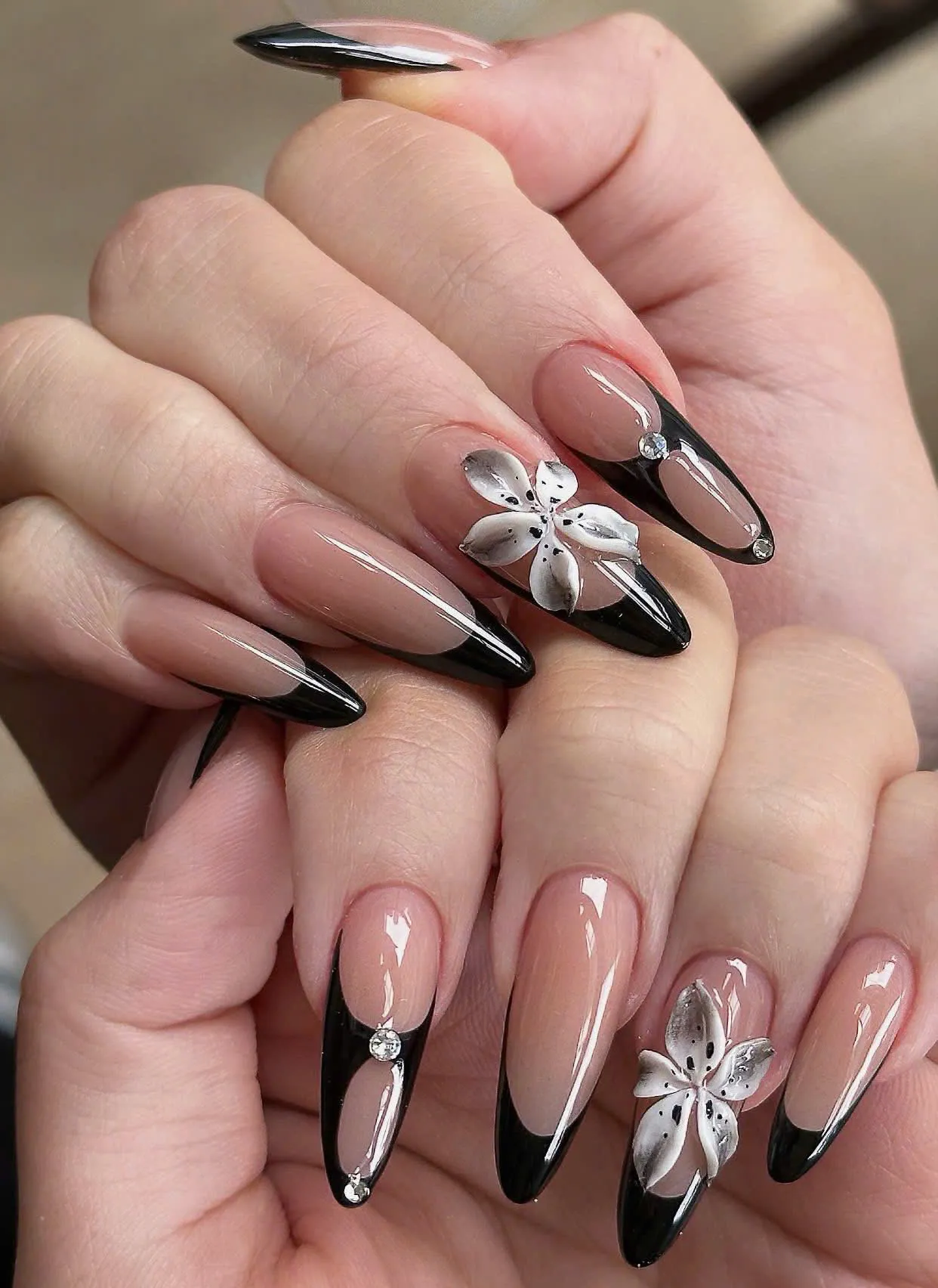 Almond nails with glossy black French tips and 3D white lily flowers